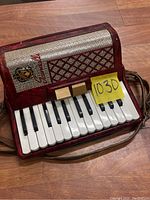 Photo showing the front of the accordion head with piano keys and buttons, maroon red body, and a yellow label with number 1030.