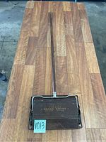 Full length view of the antique Bissell rug sweeper showing wooden handle and sweeping base.