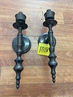 Pair of antique wall sconce candlestick holders shown from the front on a wooden surface.