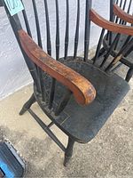 Close-up photo of chair armrest showing natural wood finish worn with age and black-painted spindles.