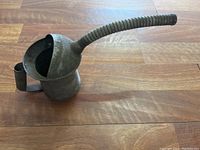 Side profile of the metal antique oil can resting on a wooden surface, showing the full length of the long flexible spout and handle.