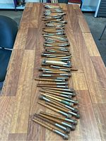 Overview of about 60 wooden thread spools laid out on a wooden table, showing variation in size and color.