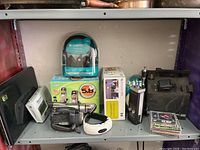 Various electronic items on a shelf including a U-lock, boxed cordless phone, CDs, cordless drill, digital thermometer, and radio receiver.