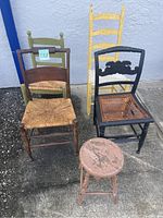 Front view of four antique chairs and one round stool showing various chair designs, seat materials, and paint conditions.