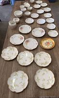 Full overview of all Haviland France china pieces arranged on table to show quantity and variety of plates, bowls, and creamers. Shows floral and gold trim details.