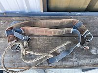 Full view of the heavy duty safety harness laid out on wooden surface showing fabric straps, rope, and metal hooks.