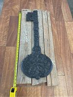 Full view of the 30 inch large rustic decorative metal key placed on wooden planks with measuring tape for scale.