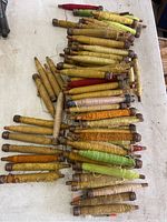 Large assortment of wooden antique thread spools with various threads in colors like yellow, orange, and green, spread on white table