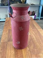 Front view of red decorative milk can with distressed paint and handles on wooden table.