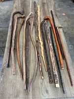 Full view of the 14 antique walking canes and sticks with variety of shapes, wood types, and finishes, spread on wooden surface.