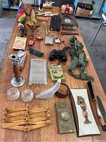Overview of all items on wooden table showing a broad collection of miscellaneous estate items including umbrella, candlestick, glassware, binoculars, belts, brushes, plaques, and small containers.