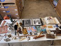 View of miscellaneous smaller items arranged on a table including fishing reels, postcards, coins, copper measuring cup, trinket box, wooden carved items, photo album and scrapbooks