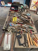 Photo of assorted hand tools laid out on table showing various pliers, wire cutters, saws, files, clamps and screwdrivers.