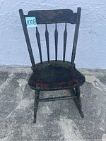 Front view of small antique rocking chair showing contoured seat, spindle backrest, and curved rockers with worn black paint.