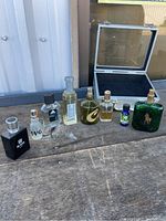 Photo showing the travel box with clear lid and eight assorted fragrance bottles in various shaped containers arranged in a row on a wooden surface.