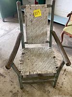 Full front view of the antique chair showing woven seat and back with solid wood limbs forming the frame and arms.