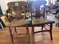 Photo of two antique hardwood chairs side by side showing cane seats and curved backrests in a workshop setting