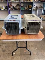 Two cat carriers on a wooden table in a warehouse setting, showing front and top views.