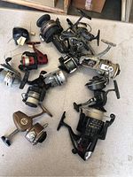 Top down view of entire lot of 11 vintage fishing reels in varied colors and condition, showing details and size differences