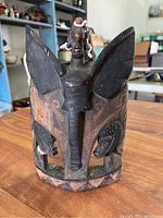 Front view of the carved wooden African statue with central winged figure and three faces on base, showing beaded decorations.