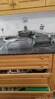 Overview of all bakeware and mixing bowls on kitchen counter with wooden cabinets and tiled backsplash.
