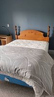 Angled view of assembled queen bed with wood headboard, mattress, box spring, and comforter