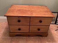 Front view of four drawer wooden dresser showing round wooden knobs and natural wood finish.