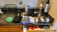 Countertop view of hardware items, metal wine bottle holder, batteries, tape measure, and more grouped