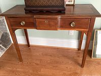 Full view of the wooden desk showing legs, single drawer with brass handles and keyhole, and top surface.
