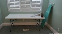 Folding table with ironing boards and iron placed to the right side, viewed from front at an angle.
