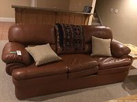 Front view of brown leather sofa with cushions and throw