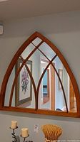 Front view of cathedral style mirror with wooden frame and mullions, hanging on wall above decorative items.