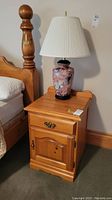 Frontal view of one nightstand next to wooden bedpost with lamp on top