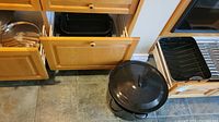 Photo showing large black speckled covered stock pot on floor, black roasting pan in open drawer, and wooden kitchen drawers.