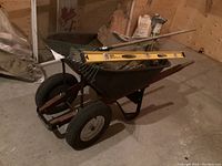 Top-down view of wheelbarrow loaded with rake and level in basement