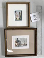 Photo showing two framed watercolor paintings side by side with a ruler for scale. The top smaller painting depicts a canal scene, the bottom larger painting depicts a cityscape of Rome.