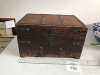 Front view of wooden trunk showing metal latch and metal strip reinforcements.
