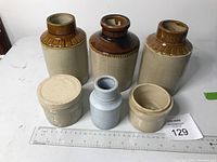 Front view of all six stoneware crocks and jars including three tall crocks with brown glazed tops, two smaller jars, and one lidded jar with embossed crossed keys and lettering.