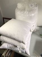 Photo shows two white lumbar pillow inserts sized approximately 22x12 inches stacked on a table with other pillow inserts.