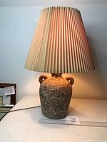 Full view of lamp showing ceramic pottery base with fat lava glaze and beige pleated lampshade.