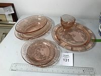 Pink depression glass items including serving bowl, cake plate, platter, two small plates, and cream pitcher on table with measuring ruler.