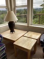 Overview photo showing three blonde wood tables in a corner by windows with a lamp on the large table.