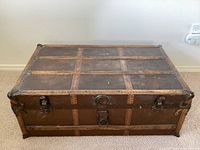 Front view of vintage wood trunk showing copper accents and leather handles with one missing handle.