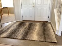 View of rectangular area rug with a blend of gray tones placed in entryway with a double white door.