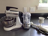 Full view of Sunbeam stand mixer with stainless steel bowl, Cuisinart food processor, and Braun immersion blender on countertop
