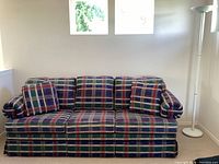 Full view of plaid hide-a-bed couch with three matching cushions and white floor lamp standing to the right, showing overall condition and style.