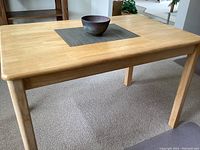 Honey-colored wood table showing surface and legs, with some visible light scuffs and slight discoloration.