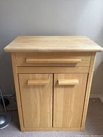 Front view of small light wood kitchen cabinet with drawer above double doors closed.