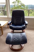 Full view of navy blue leather recliner and matching ottoman on circular wood bases