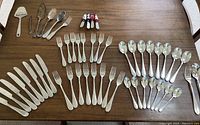 Flatware arranged on table showing knives, forks, teaspoons, tablespoons, lighthouse spreaders, and miscellaneous pieces.